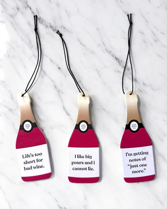 Three wine bottle-shaped tags with humorous text on a marble background