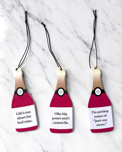 Three wine bottle-shaped tags with humorous text on a marble background