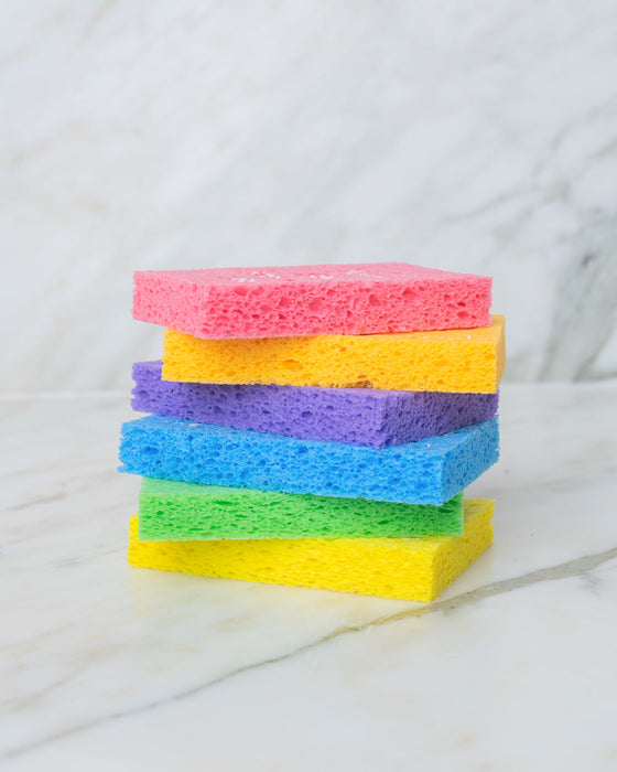 stack of biodegradable eco friendly compressed pop up sponges on counter in rainbow multi color stack. white kitchen counter.