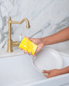 yellow kitchen sponge washing dishes in sink. sponge has a wine bottle print. biodegradable compressed kitchen sponge.