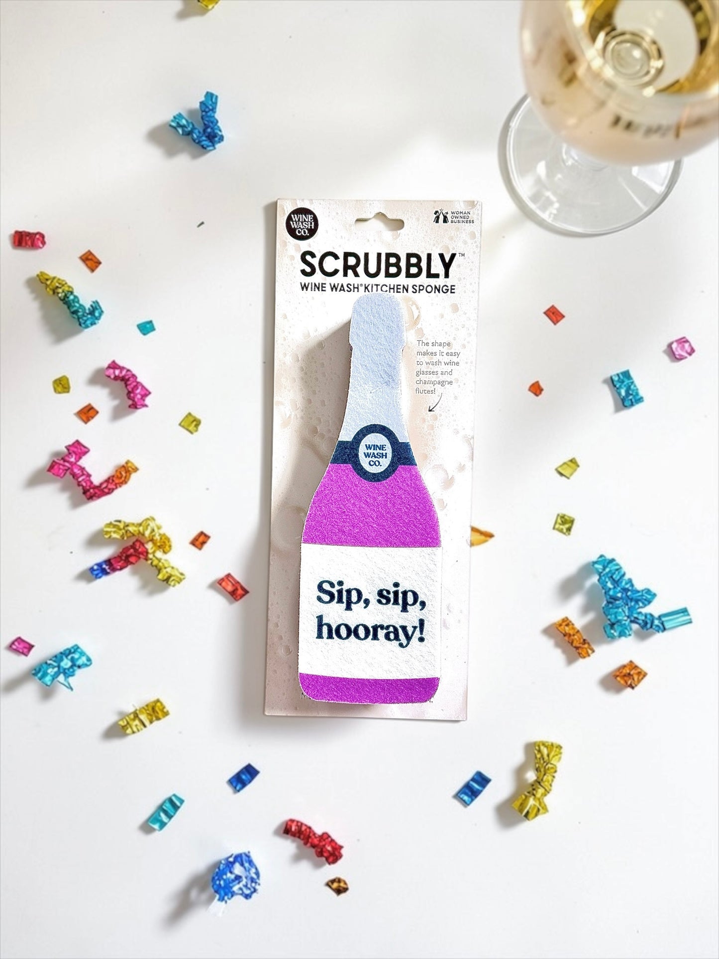Scrubbly wine wash kitchen sponge purple sip sip hooray with confetti on a white background and glass of champagne wine